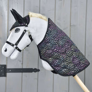 The Set Dreamy hobby horse by Hobby Horse LarDen, featuring a white body, black bridle and ears, plus a colorful dotted blanket, is shown against a gray wooden wall.
