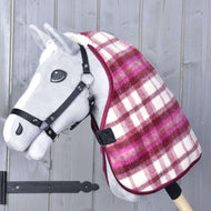 Hobby Horse giocattolo grigio con briglia nera che indossa la Coperta Stalla LarDen rossa e bianca a quadri di Hobby Horse LarDen sul collo. Sullo sfondo una parete di legno con assi verticali.