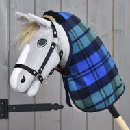 Hobby Horse LarDen con testa in tessuto grigio, briglia nera, criniera chiara, occhio e narice dipinti, che indossa la Coperta da Scuderia Perth a quadri blu e verdi. In piedi davanti a uno sfondo in legno.