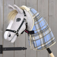 Hobby Horse di peluche con muso grigio, criniera bianca e briglia nera che indossa la Hobby Horse LarDen Coperta da Scuderia Azzurro Chiaro, montato su bastone di legno davanti a una parete rustica in legno.