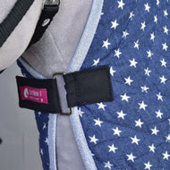 Primo piano della Coperta da scuderia Star trapuntata blu di Hobby Horse LarDen, con stelle bianche, cinghia nera con fibbia argentata e etichetta rosa Izefan, indossata da un animale grigio come parte della sua pettorina o del suo gilet.