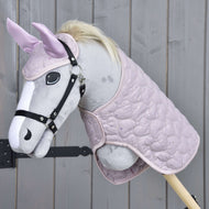 Hobby Horse LarDen Set Cuore Più Dolce con Hobby Horse in peluche dal muso grigio chiaro, briglia nera, criniera chiara, orecchie rosa con cuffia per orecchie e coperta trapuntata rosa, esposto su sfondo in legno.