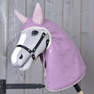 Hobby Horse LarDen "Raincoat Sweetheart", Hobby Horse in peluche con muso grigio, briglia nera, orecchie rosa e impermeabile lavanda con stampa a cuori, perfetto per ogni condizione meteo, montato su un bastone di legno davanti a una parete di legno.