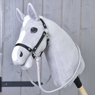 Hobby Horse LarDen Reins Tizian con Hobby Horse in peluche grigio, briglia nera e redini artigianali su un bastone di legno, fotografato davanti a uno sfondo di pannelli in legno chiaro.