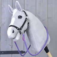 Hobby Horse LarDen Redini Viola con Hobby Horse grigio, lista bianca, briglia nera e vivaci redini artigianali, con testa in peluche su bastone robusto e mostrato davanti a una staccionata in legno chiaro.