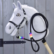Hobby Horse - Lunghina Rainbow di Hobby Horse LarDen, Hobby Horse grigio con criniera bianca, briglia nera, redini e lunghina con nastro rainbow intorno al collo, esposto davanti a pannelli di legno.