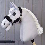 Hobby Horse LarDen con cavezza nera con pelliccia nera completa in similpelle e bastone di legno, fotografato davanti a pannelli in legno.