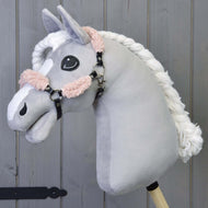 Cavezza nera con pelliccia Old Rose completa - similpelle di Hobby Horse LarDen su un Hobby Horse in peluche con testa grigio chiaro, criniera bianca intrecciata e cavezza nera, montato su un bastone di legno davanti a pannelli in legno.