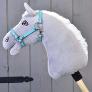 Cavezza - similpelle nera (taglia S) di Hobby Horse LarDen su Hobby Horse di peluche grigio con criniera bianca e briglia blu, montato su bastone in legno davanti a pannelli di legno grigio.