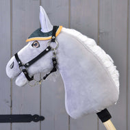 A gray plush Hobby Horse LarDen with a white mane, black bridle, and an Ear Bonnet Thermo Sport in green and yellow sits on a wooden stick in front of a gray wooden wall.