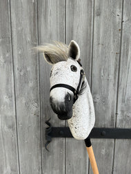 Hobby Horse Luna con capezza nera - taglia S di Hobby Horse LarDen mostrato su un bastone davanti a una recinzione di legno invecchiata con venature visibili e un gancio in metallo.