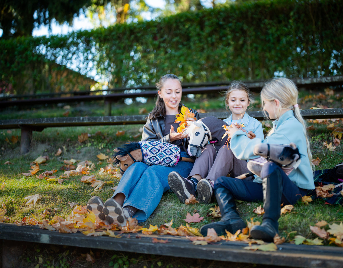 Tre ragazze con i loro Hobby Horse sui gradini autunnali coperti di foglie