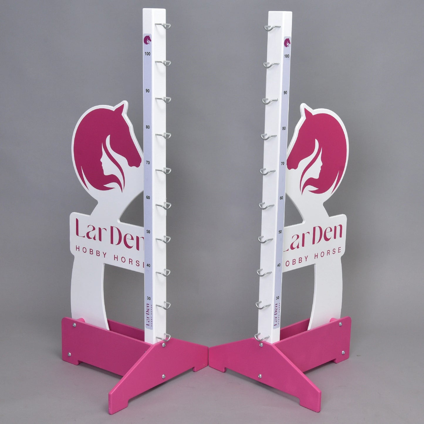 Due supporti LarDen jump 110 cm / 43 inch rosa e bianchi di Hobby Horse LarDen con disegni di teste di cavallo, indicatori di altezza regolabile e supporti metallici per la barra, su sfondo grigio. Sulla base è stampato "LarDen HOBBY HORSE".