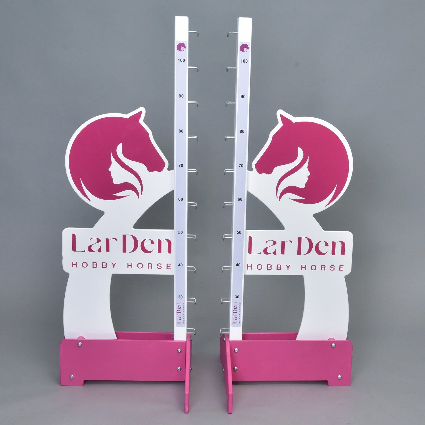 Due supporti LarDen jump 110 cm / 43 inch bianchi e rosa di Hobby Horse LarDen, con altezza regolabile fino a 110 cm, grafiche di teste di cavallo e testo del marchio sulla base, perfetti per cavalcare con Hobby Horse, mostrati su sfondo grigio uniforme.