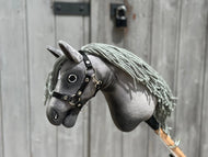 Hobby Horse Little Prince con capezza nera - taglia XS di Hobby Horse LarDen, uno stallone Hannover grigio con capezza nera e lunga criniera grigia in filato, mostrato davanti a una porta di legno invecchiata.
