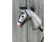 Hobby Horse Midnight Blue con capezza nera - taglia S di Hobby Horse LarDen montato su un bastone di legno ed esposto davanti a una porta di legno invecchiata.