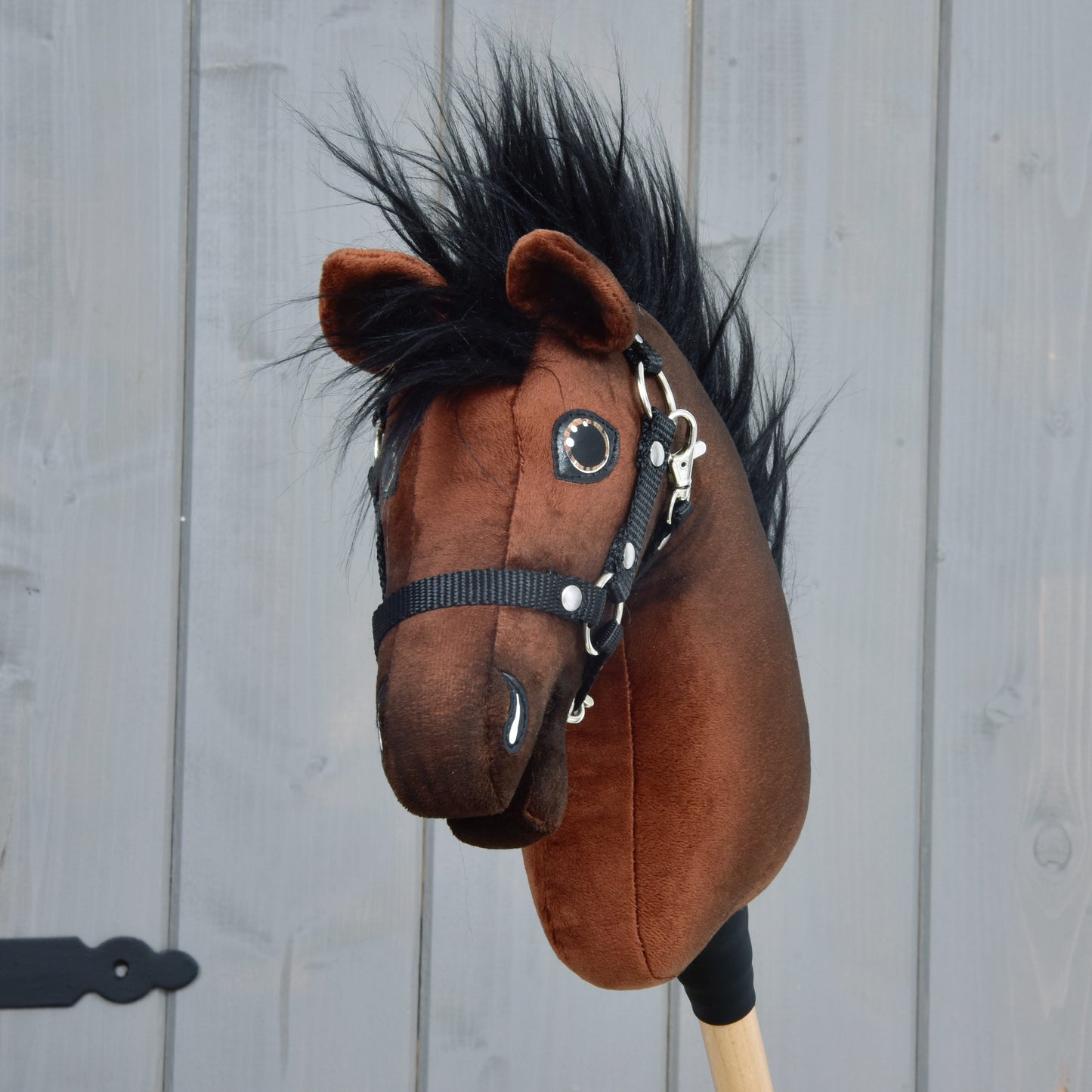 The Hobby Horse LarDen "Hobby Horse Benny with Black Halter" (size XS) features a brown head, black mane, and black halter on a wooden stick, shown against a light gray wooden background.