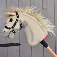 Hobby Horse Ivory Dream con cavezza nera - taglia XS di Hobby Horse LarDen, con morbido pelo color avorio e manico in legno, appoggiato a una parete di legno grigia.