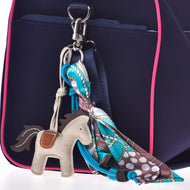 Portachiavi Horse Grey di Hobby Horse LarDen in primo piano su una borsa blu navy con finiture rosa, con una sciarpa colorata a fantasia legata a fiocco a uno degli anelli metallici della borsa.