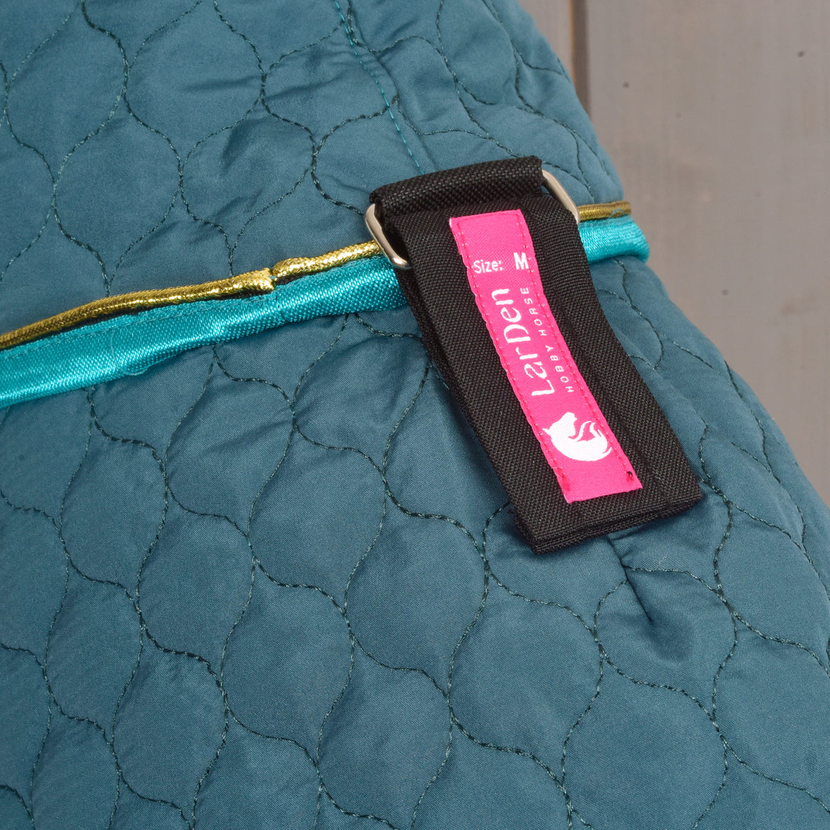 Dettaglio della Coperta Hobby Horse verde trapuntata con bordo turchese ed etichetta LarDen di chiusura