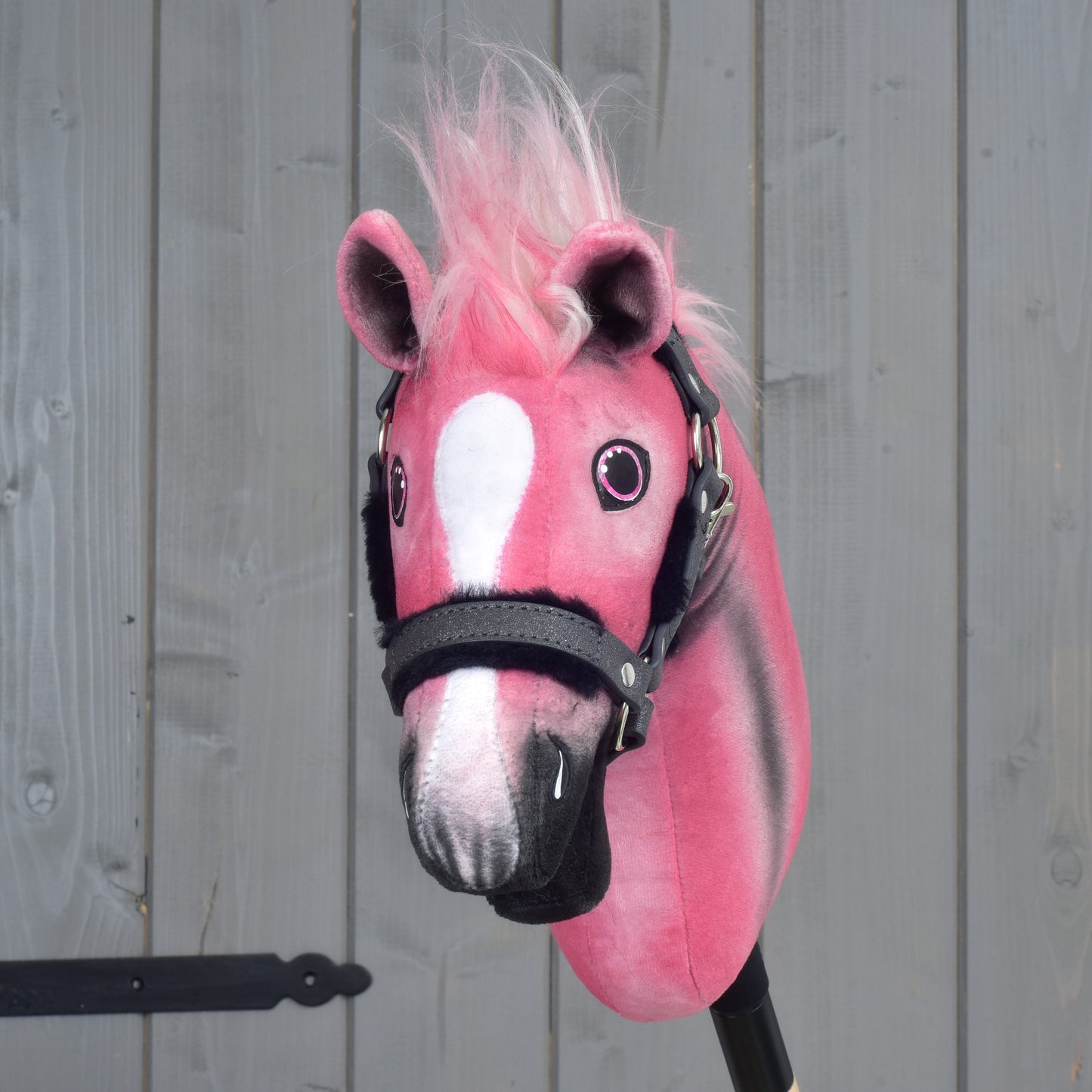 A limited edition Hobby Horse LarDen Pinkie with a glittery halter, featuring pink and white plush fur and a fluffy pink mane, is positioned against a gray wooden background.
