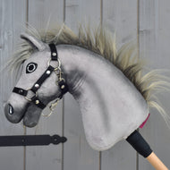 Hobby Horse Prestige con cavezza nera, taglia XS di Hobby Horse LarDen, testa in peluche grigia per Hobby Horse ispirata all'eleganza di un cavallo sportivo English Warmblood. Presenta un muso espressivo ricamato, una criniera selvaggia e una cavezza nera ben fissata, montata su un manico in legno. Posizionato su sfondo in legno, ideale per avventure imaginative di salto ostacoli.