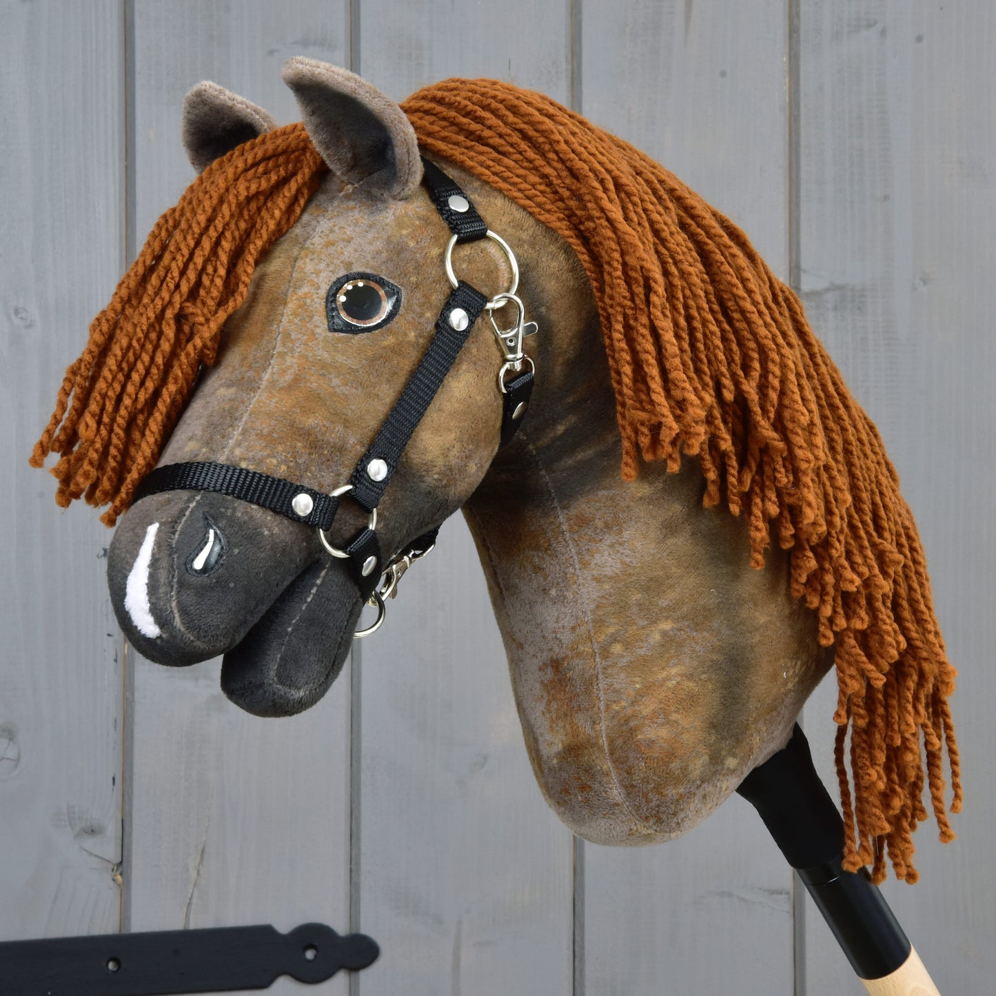 The Hobby Horse LarDen Rafaello with Black Halter (size S) features a handmade brown fabric head, black halter, and long yarn mane, pictured against a gray wooden background.