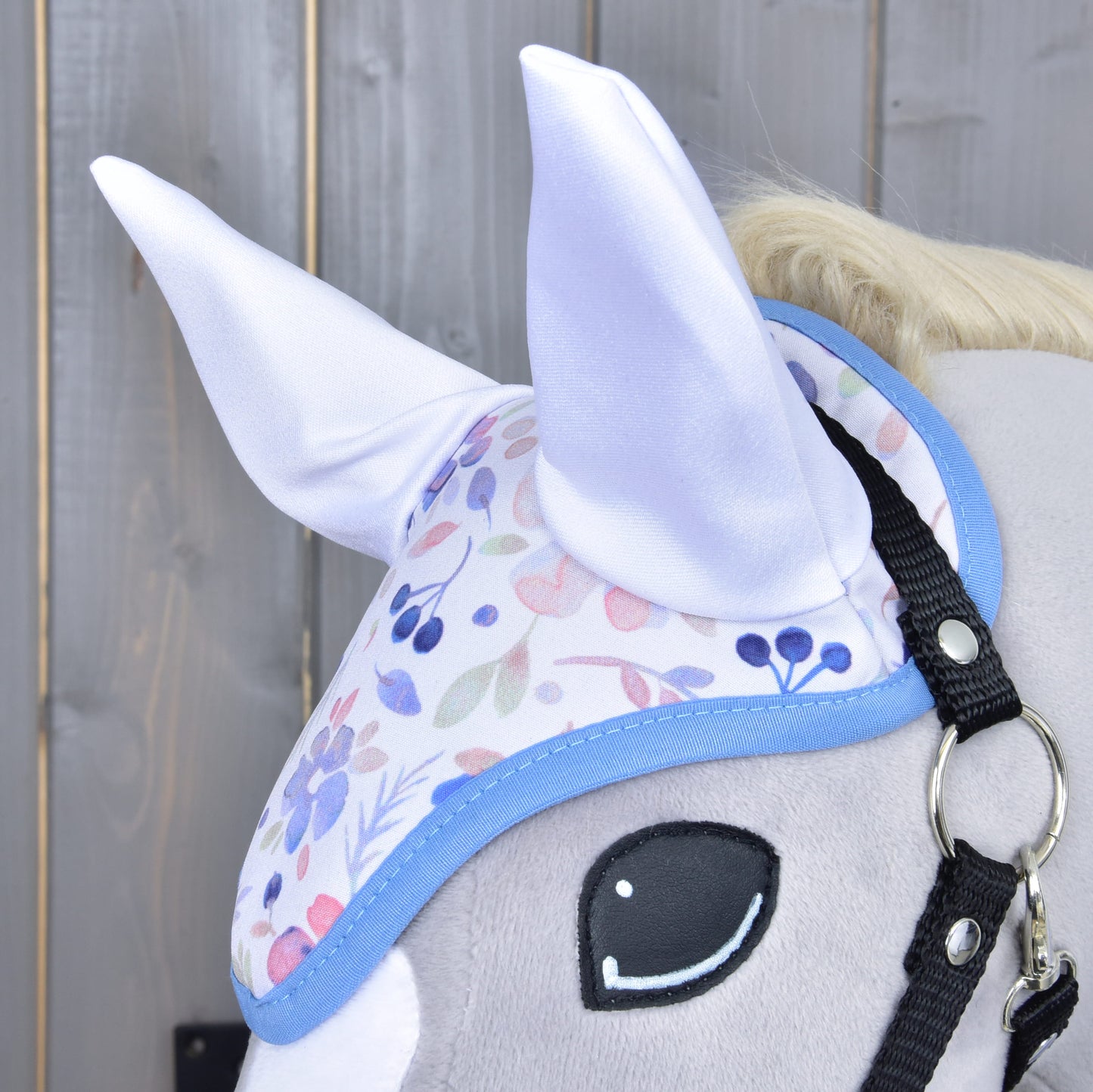Primo piano del Set Vanessa NEW di Hobby Horse LarDen: testa di Hobby Horse in peluche con cuffietta floreale pastello con morbide orecchie bianche, mostrata su sfondo in legno.