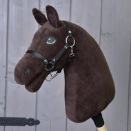 The Build your horse plush, dark brown customizable hobby horse head by related_to_12441055625556 has a black bridle, is mounted on a wooden stick, and shown against a gray wooden wall background.