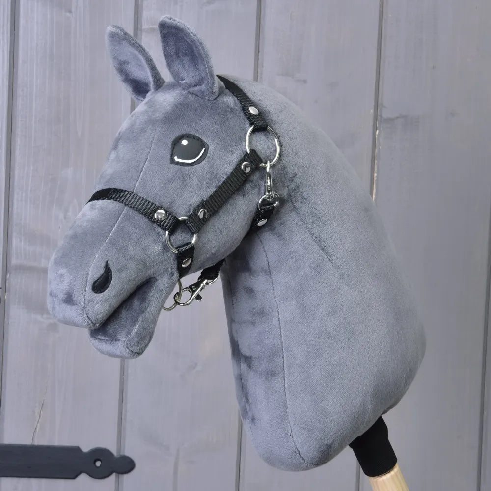 Costruisci il tuo cavallo di related_to_12441055625556, Hobby Horse personalizzabile con testa in peluche grigio scuro, briglia nera e bastone di legno, mostrato davanti a uno sfondo di assi di legno verticali.