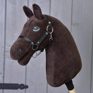 The Build your horse by related_to_12441055625556 is a custom dark brown hobby horse head with a black bridle and black faux fur mane on a wooden stick, shown in front of a gray wooden door.