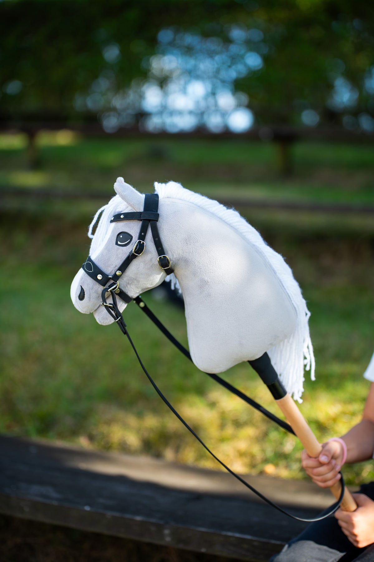 Detail photo: the head and neck of the Hobby Horse Popcorn with Black Halter by Hobby Horse LarDen held up in a sunlit garden - white plush, white yarn mane and forelock - shown here with the decorated bitless bridle.