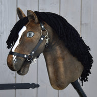 Hobby Horse Sundance con cavezza nera di Hobby Horse LarDen, con testa marrone ispirata alla velocità degli stalloni, criniera nera in filato, lista bianca e cavezza nera, montato su un robusto bastone di legno davanti a una parete di legno grigia.